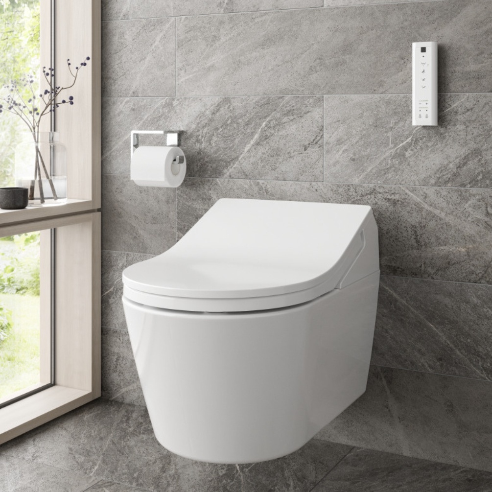 Lifestyle image of the TOTO Washlet RX Auto Flush Rimless Wall Hung Toilet mounted on a grey bathroom wall next to a toilet roll holder and the Washlet remote control